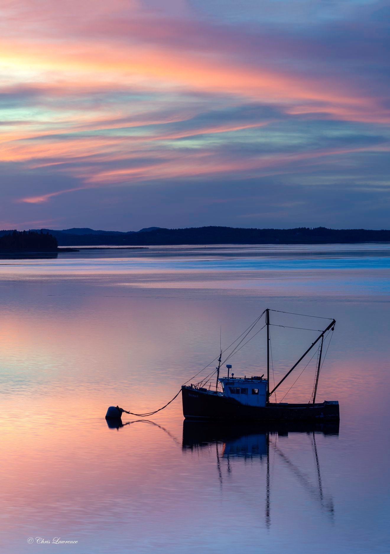 A Maine fishing boat moored on glassy water at a dramatic pink and purple sunset